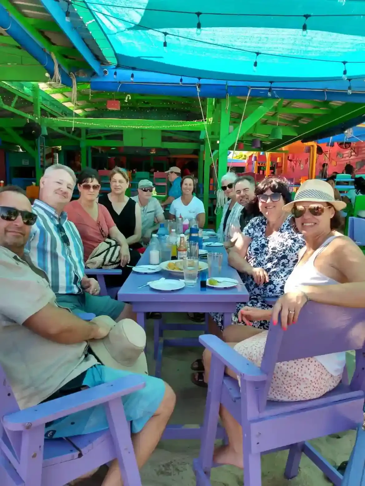 A group of people enjoying the Lunch Walking Food Tour at a vibrant purple outdoor café table surrounded by colorful decor.