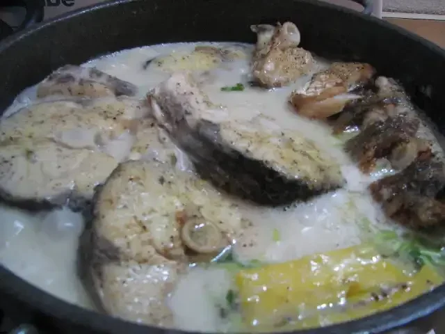 Fish stew with thick slices of fish in a creamy broth, seasoned with herbs and spices, cooking in a pan.