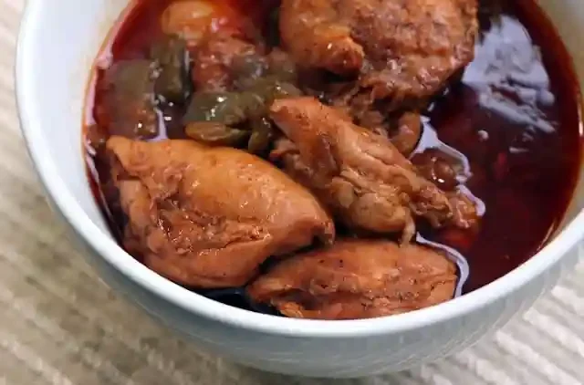 A bowl of chicken stew with chunks of chicken and vegetable pieces in a rich, reddish broth.